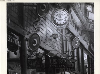 Signs for C.P. Reber Optician, Burnstine Caster Clocks, and Brooks Hats Along Their 612-614 Olive Street Store Fronts by Charles Clement Holt